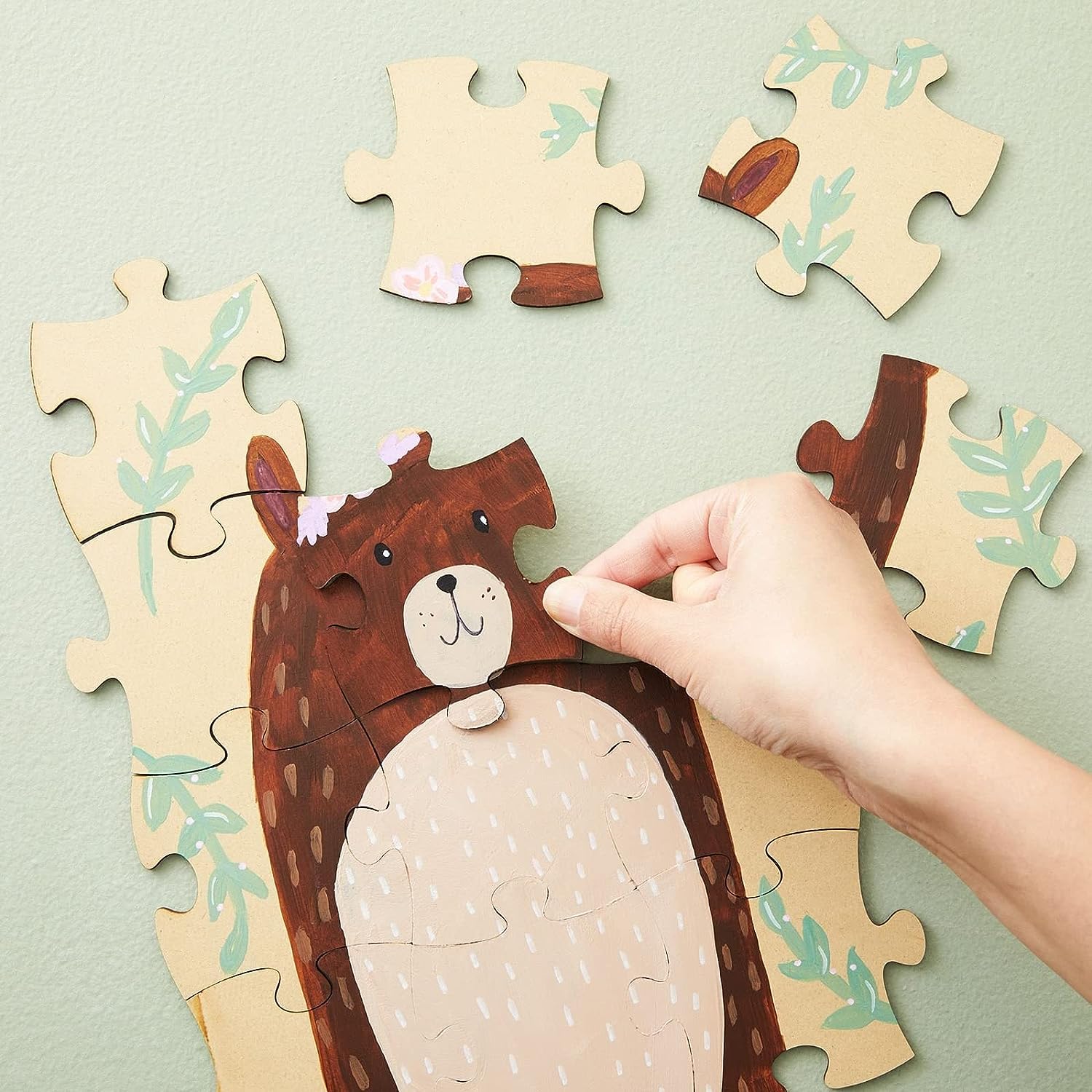 Hand assembling a wooden puzzle of a bear with a light green background