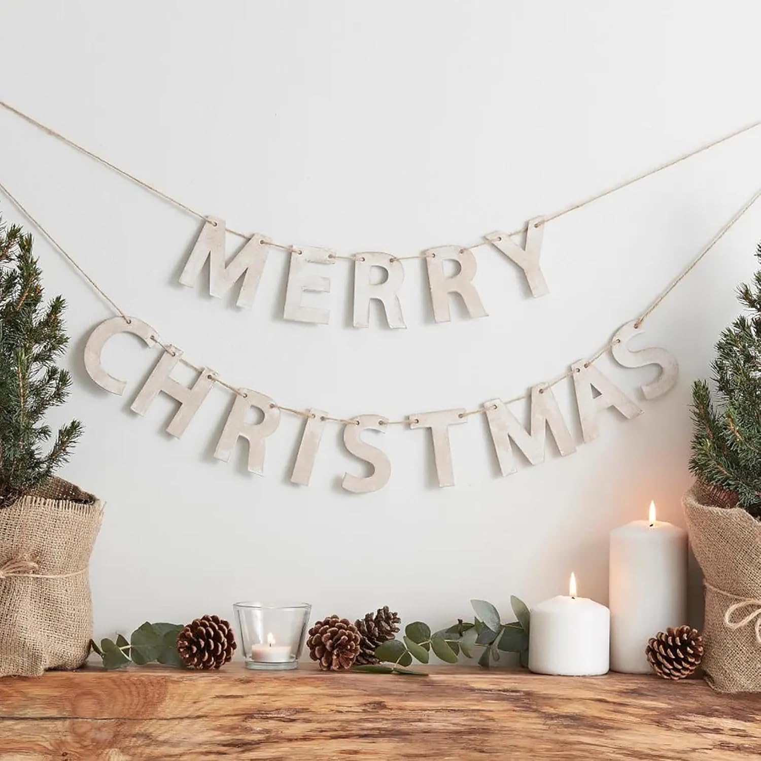 Merry Christmas banner with candles and pinecones on a wooden surface.