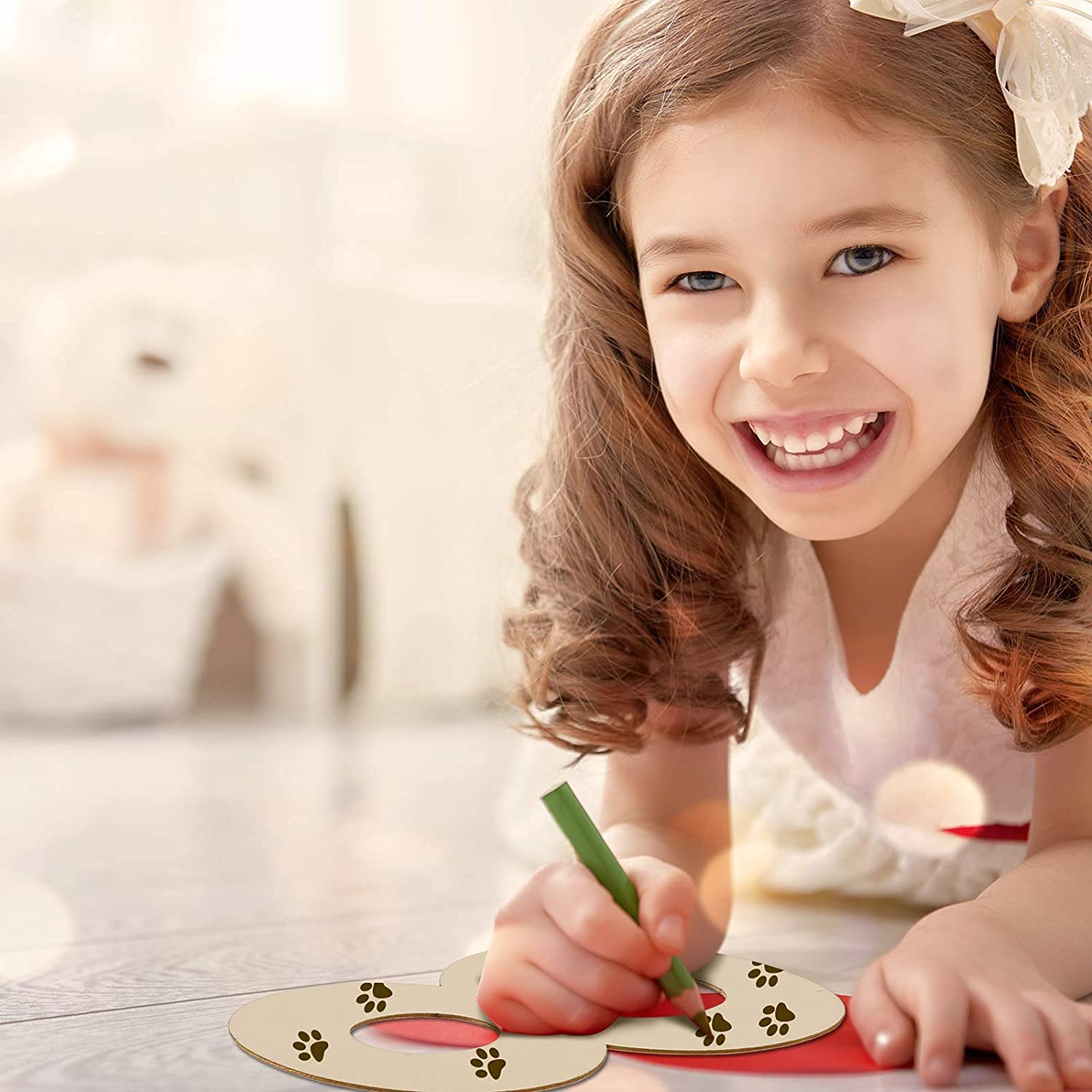 Young girl smiling while painting with a brush on a wooden surface.