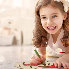 Young girl smiling while painting with a brush on a wooden surface.