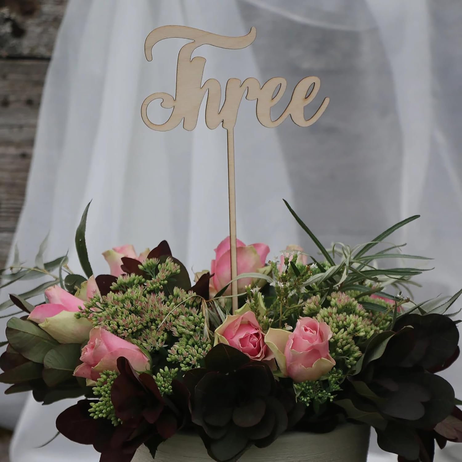 Floral arrangement with a wooden 'Three' cake topper on a blurred background