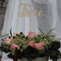 Floral arrangement with a wooden 'Three' cake topper on a blurred background