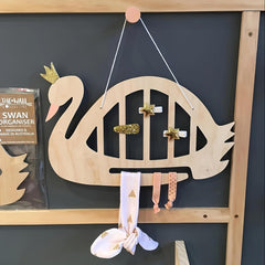 Wooden swan-shaped organizer with decorative items on a dark wall