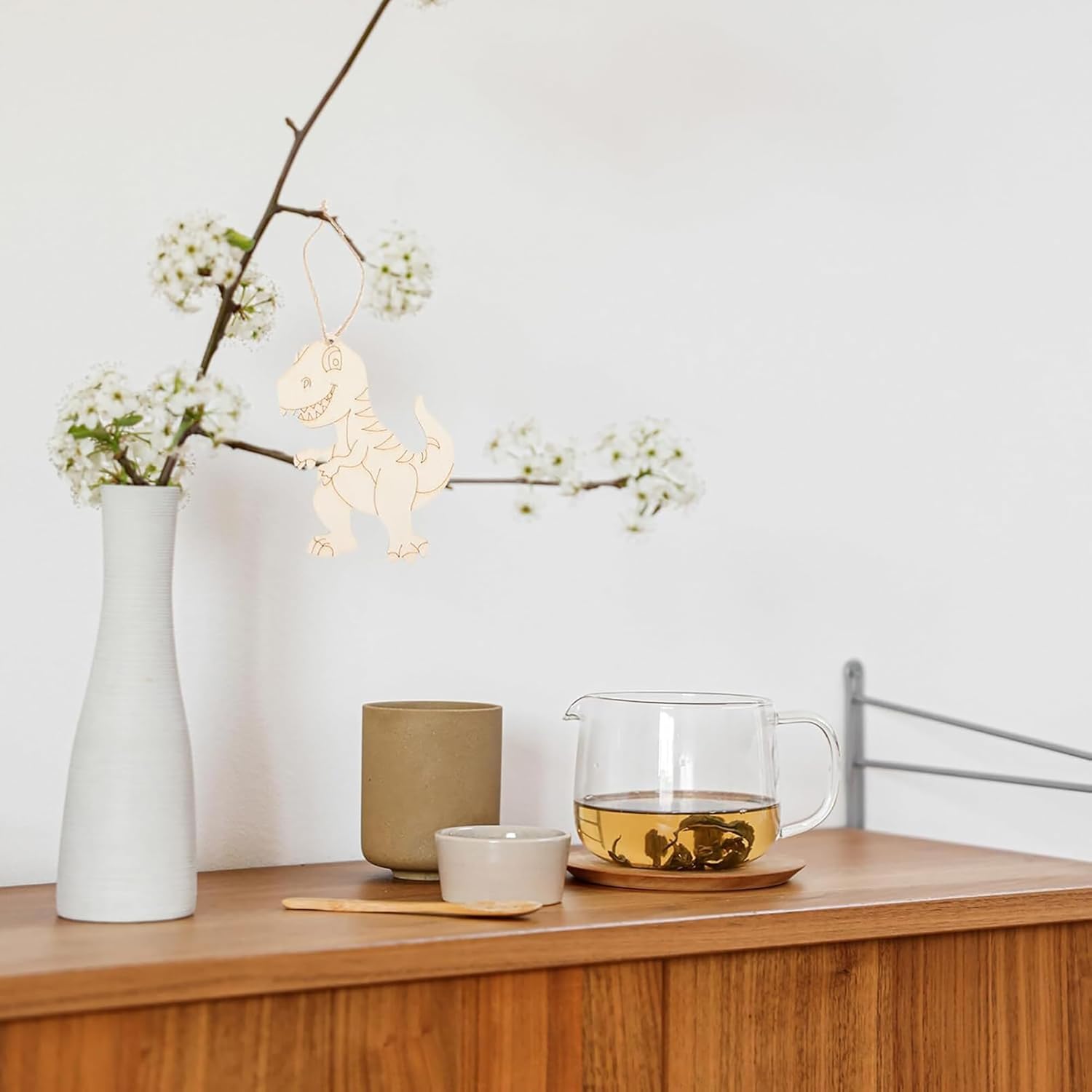 Tea set with a glass teapot, ceramic cups, and a vase on a wooden surface.