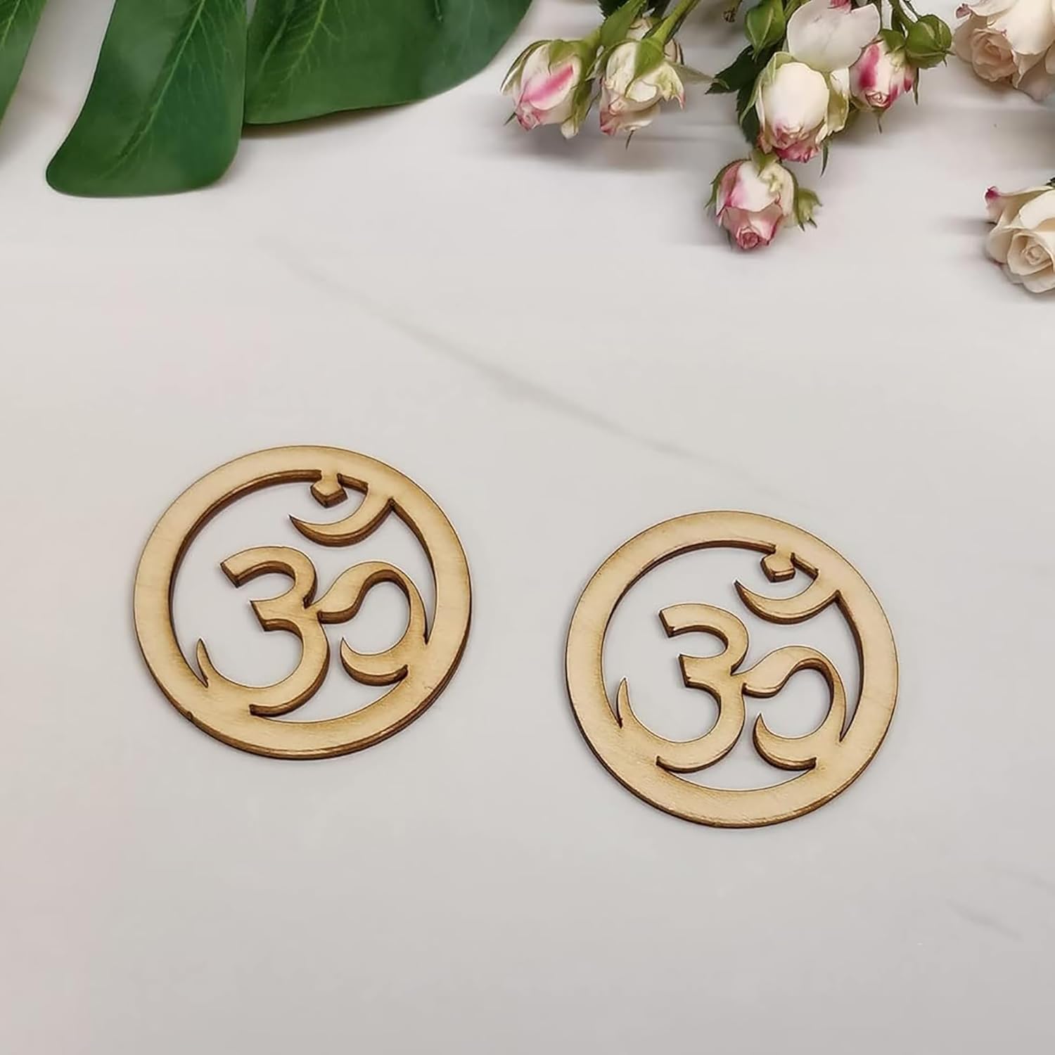 Two wooden om symbol coasters on a light surface with flowers in the background