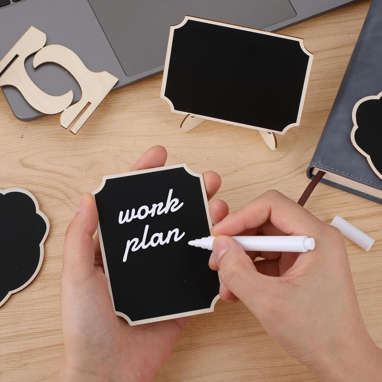 Person writing 'work plan' on a small blackboard with markers on a wooden surface.