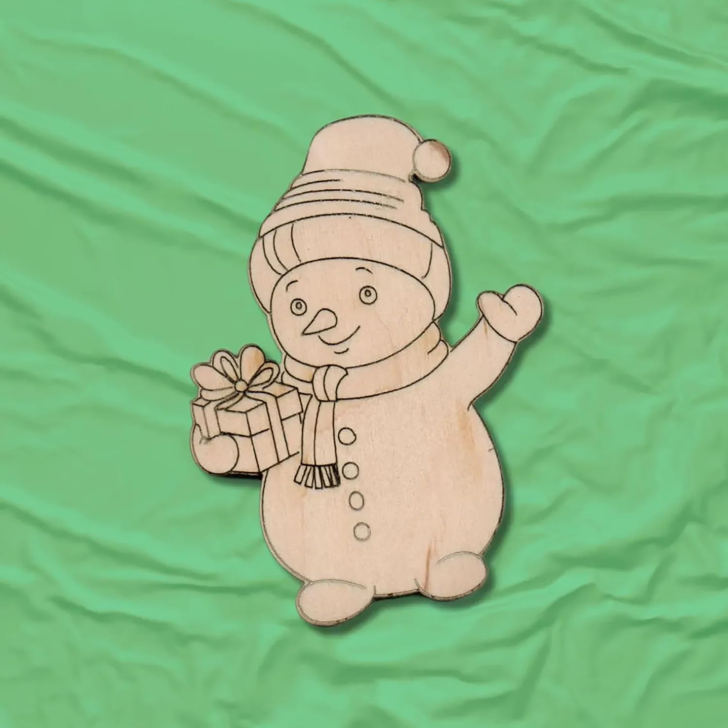Wooden snowman ornament with a gift on a green fabric background