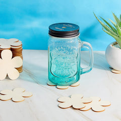 Clear glass jar with handle and black lid on a white surface with decorative items.