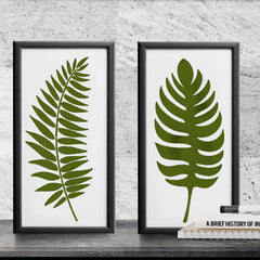 Two framed prints of green leaf designs on a concrete wall.
