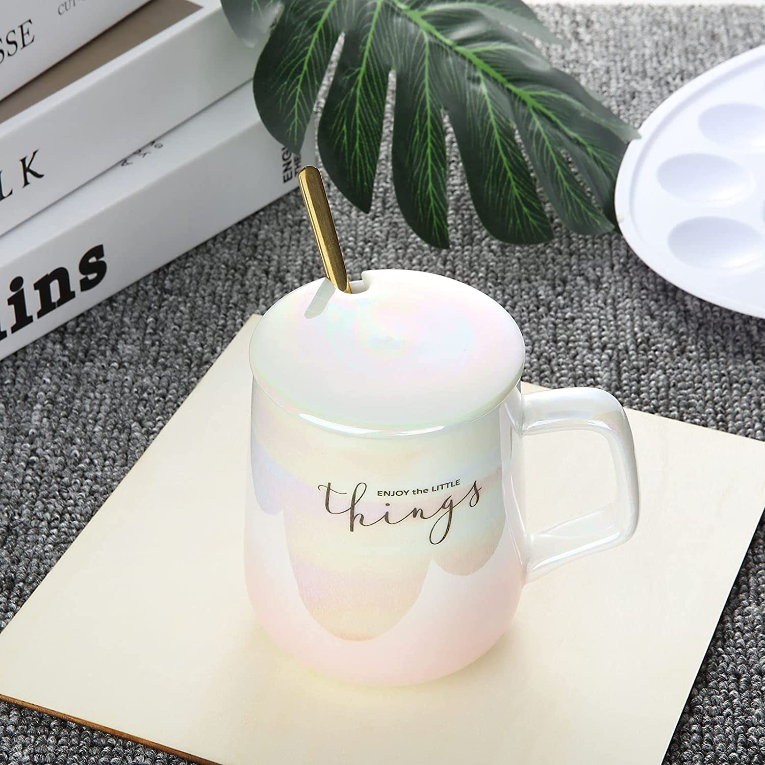 Iridescent mug with a spoon on a textured surface with books and a plant in the background