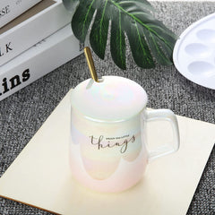 Iridescent mug with a spoon on a textured surface with books and a plant in the background