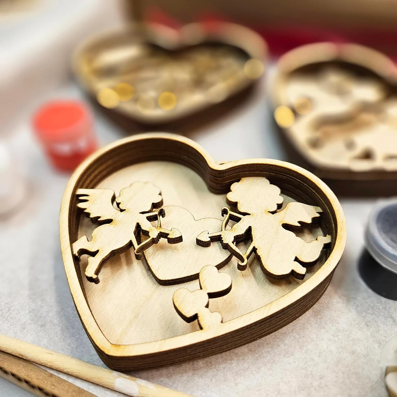 Wooden angel figures in a heart-shaped box on a light surface