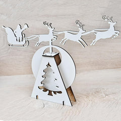 Decorative Christmas scene with Santa in sleigh, reindeer, and tree on a light wooden background