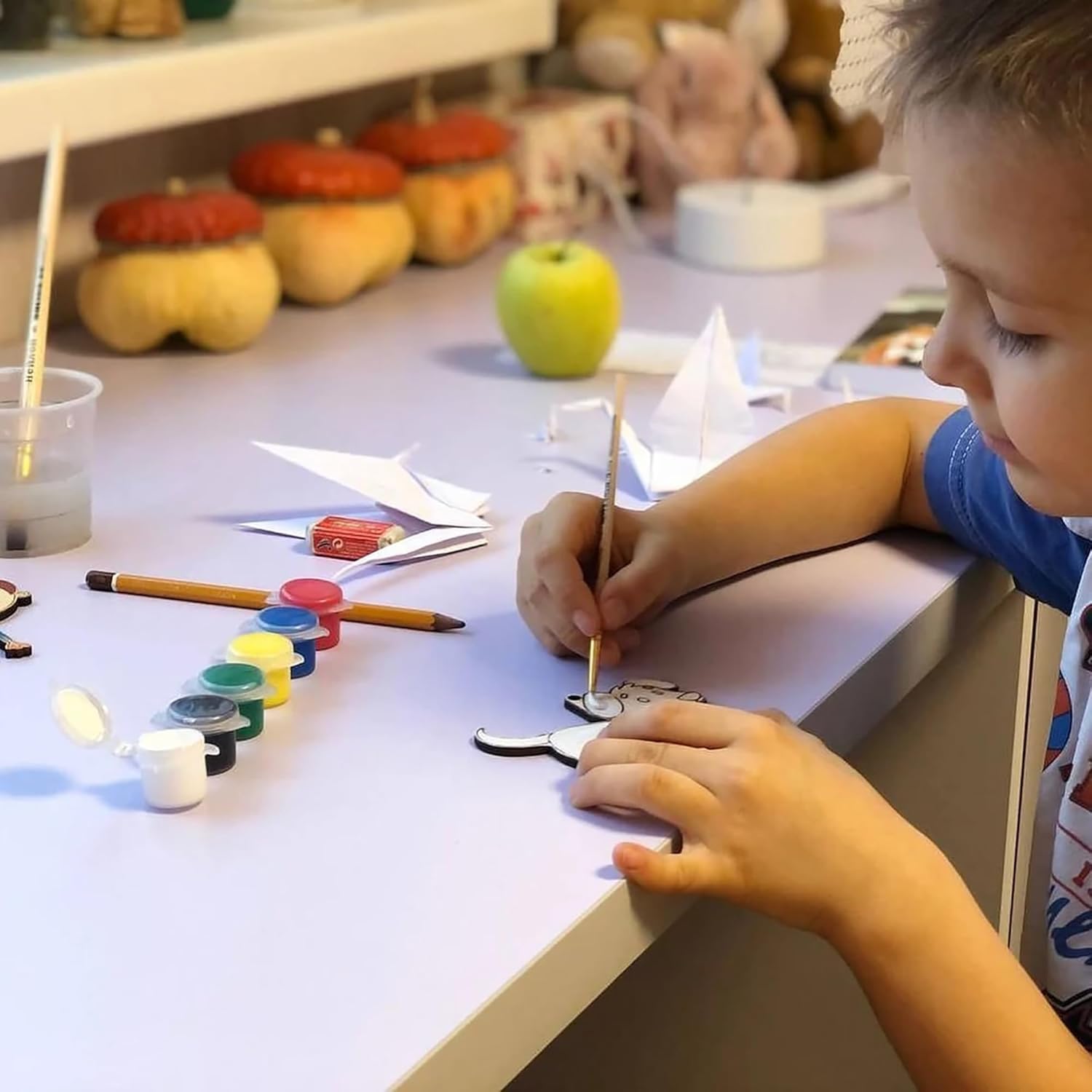 Child painting a small object at a table with art supplies