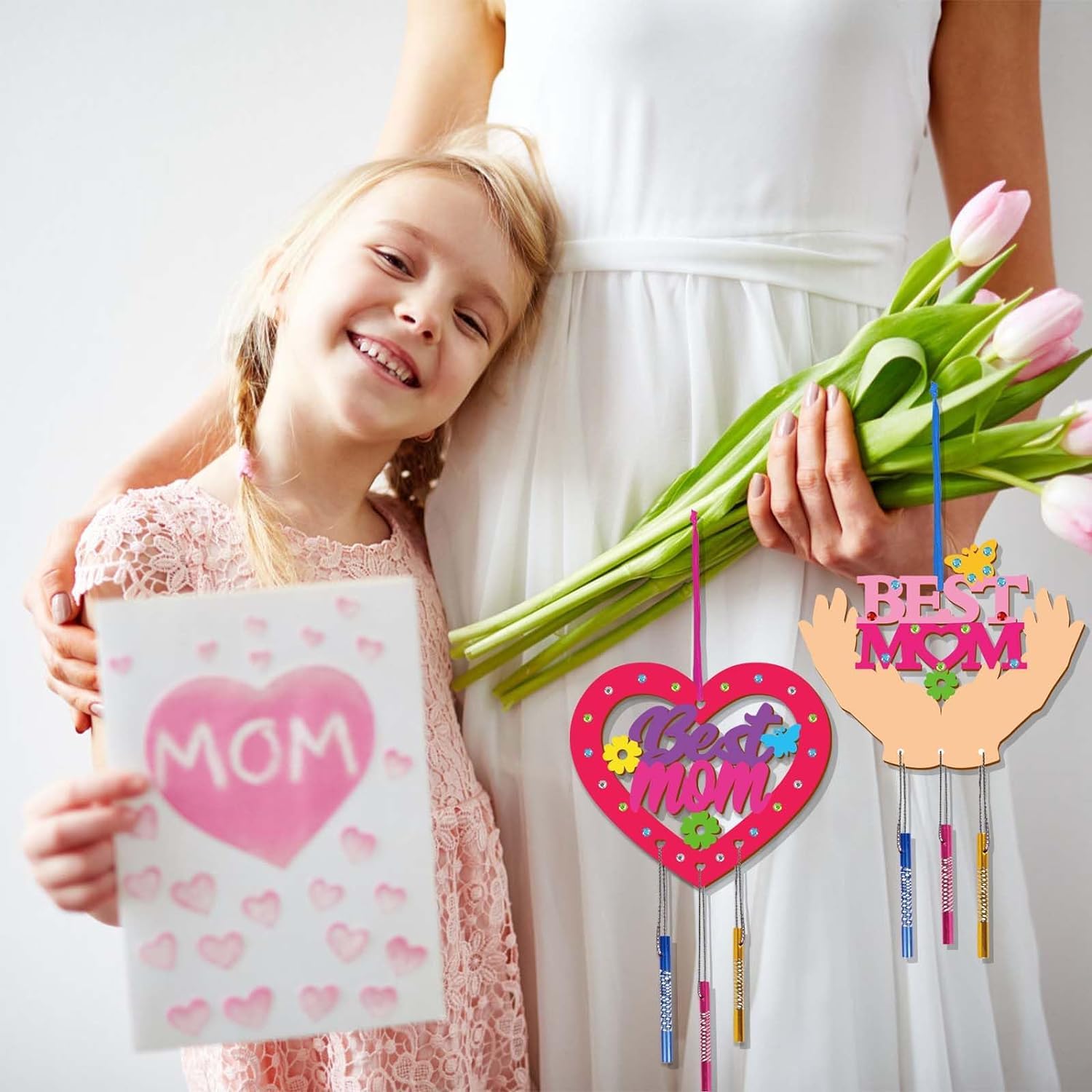 Child holding a 'MOM' card with a woman holding tulips, with decorative items in the foreground.
