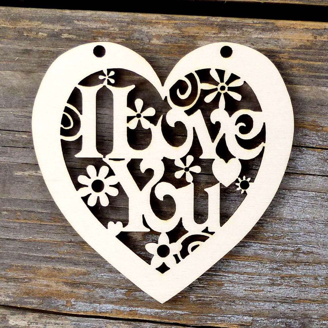 Heart-shaped decorative cutout with floral and swirl designs on a wooden background