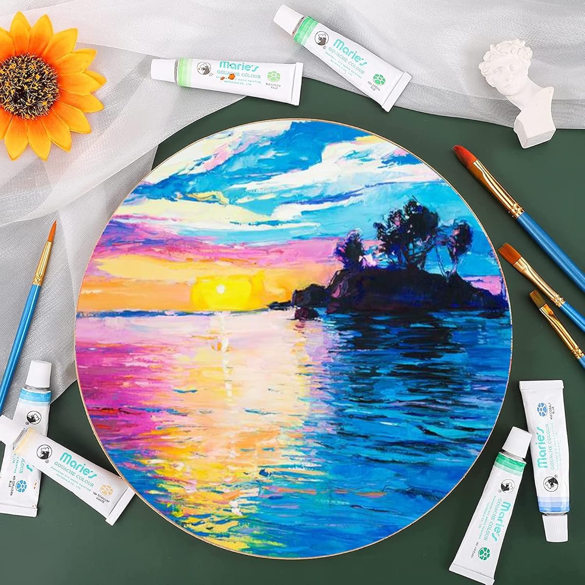 Painting of a sunset over water with art supplies on a green surface