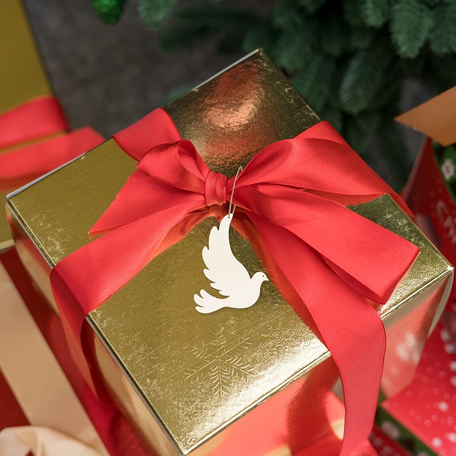 Gold gift box with a red ribbon and dove tag, surrounded by Christmas decorations.