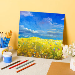 Painting of a field with flowers on a yellow background, surrounded by art supplies.