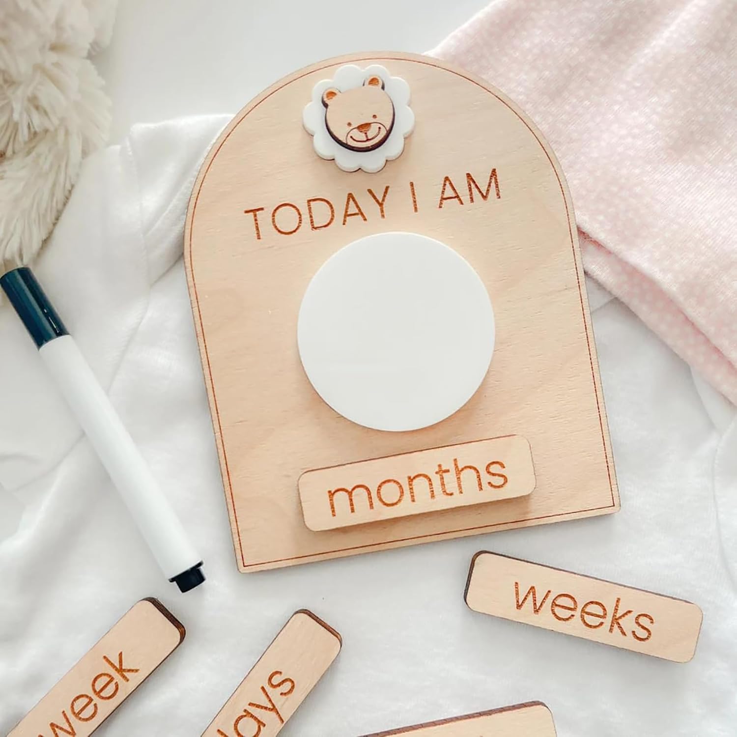 Baby milestone board with wooden cards for tracking days, weeks, and months on a soft surface.
