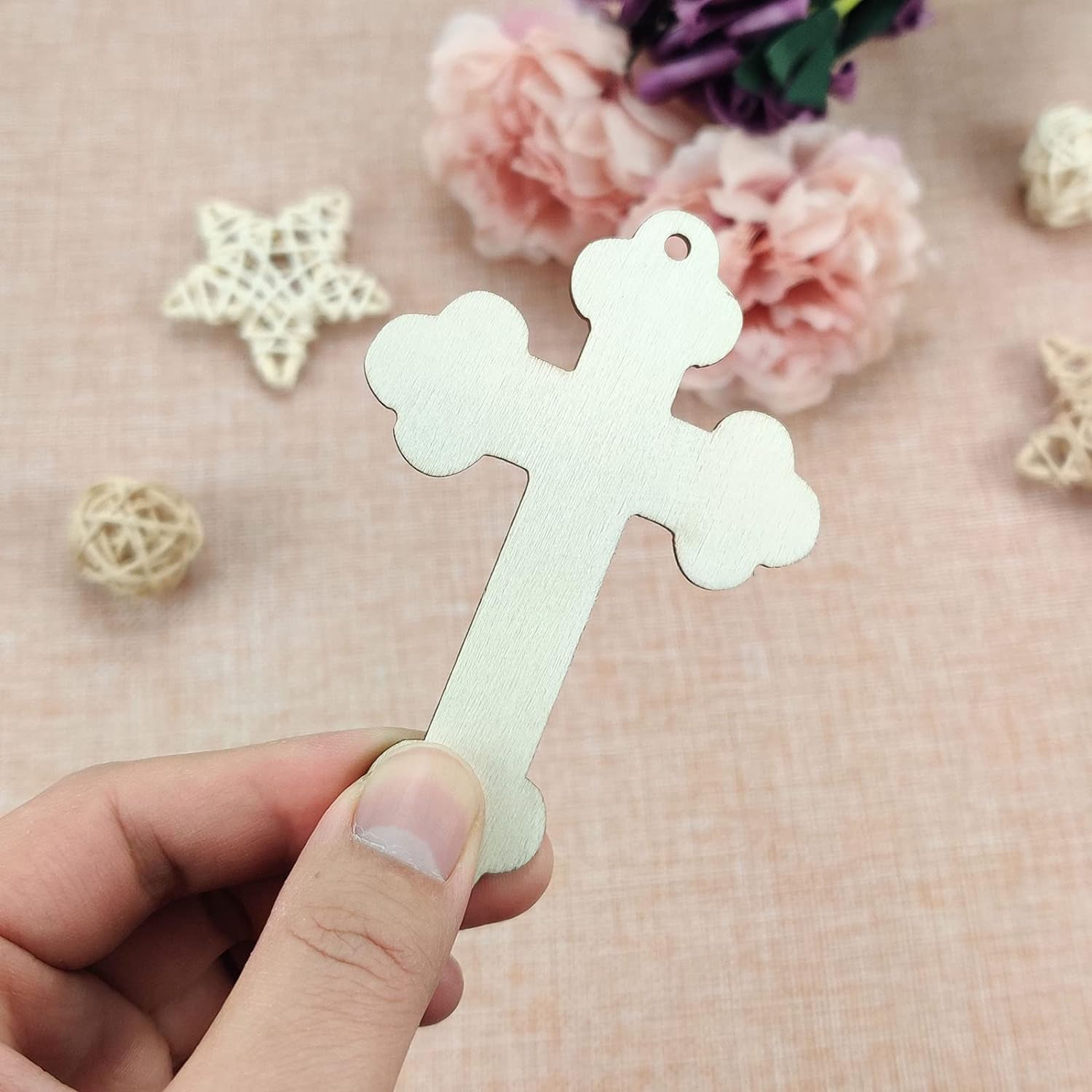 White cross-shaped tag held by a hand with a soft pink background and decorative elements.