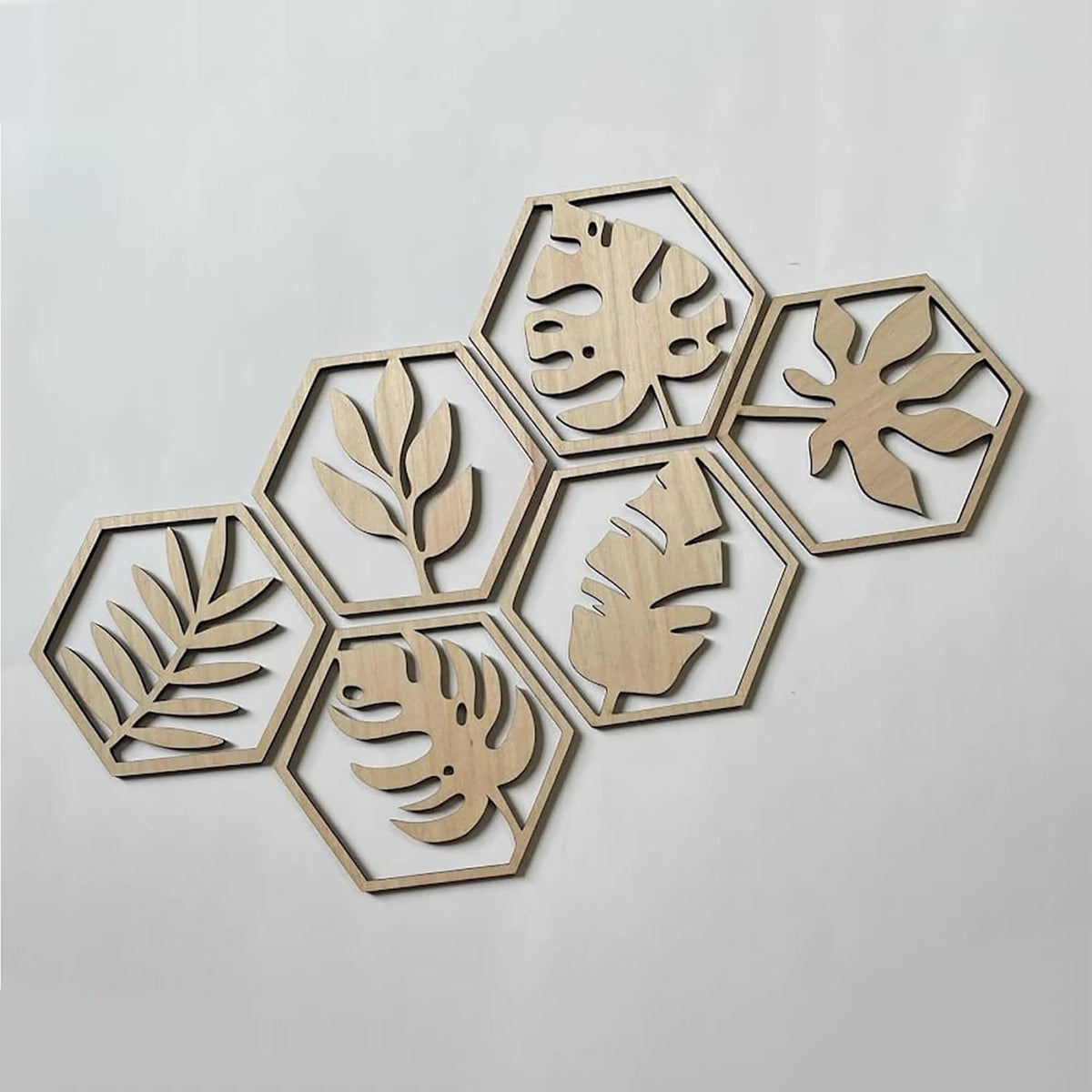 Hexagonal wooden wall art pieces with leaf patterns on a light gray background