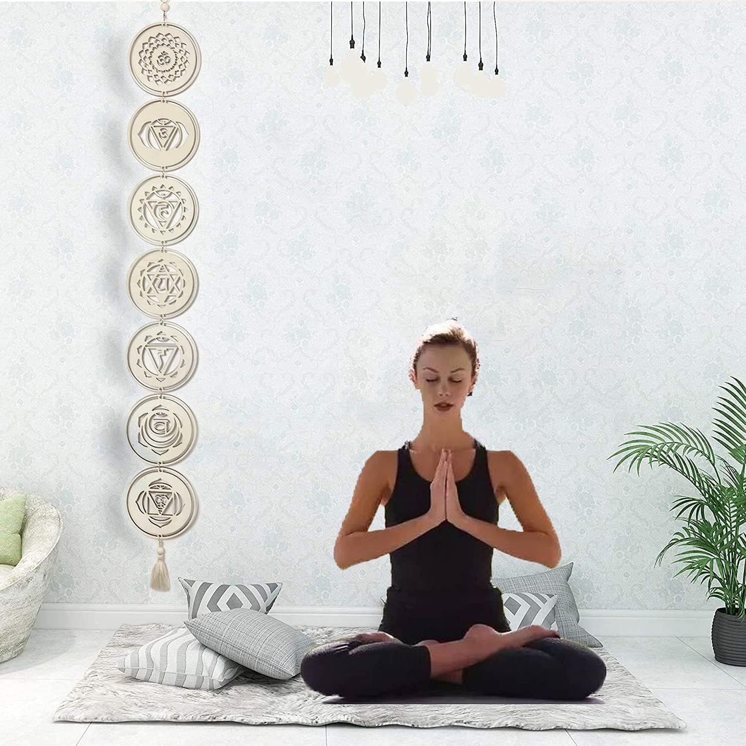 Woman meditating in a room with a wall hanging featuring chakra symbols.
