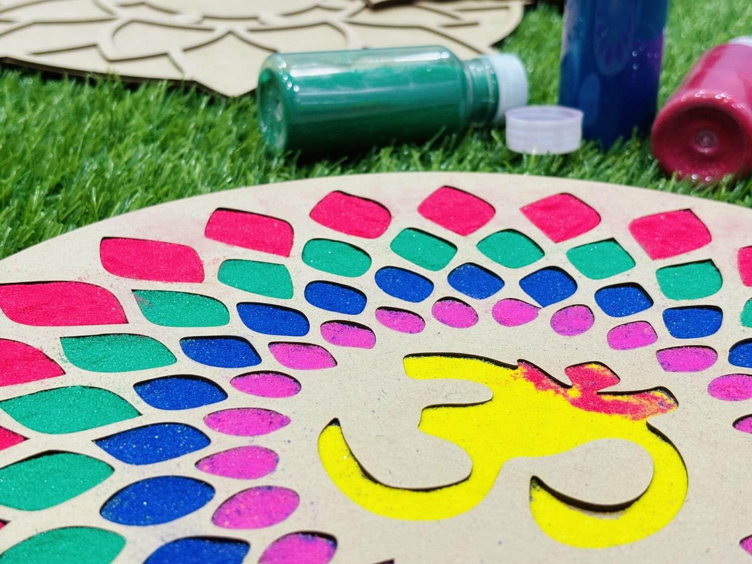 Colorful patterned board with a hand design on grass, surrounded by art supplies.