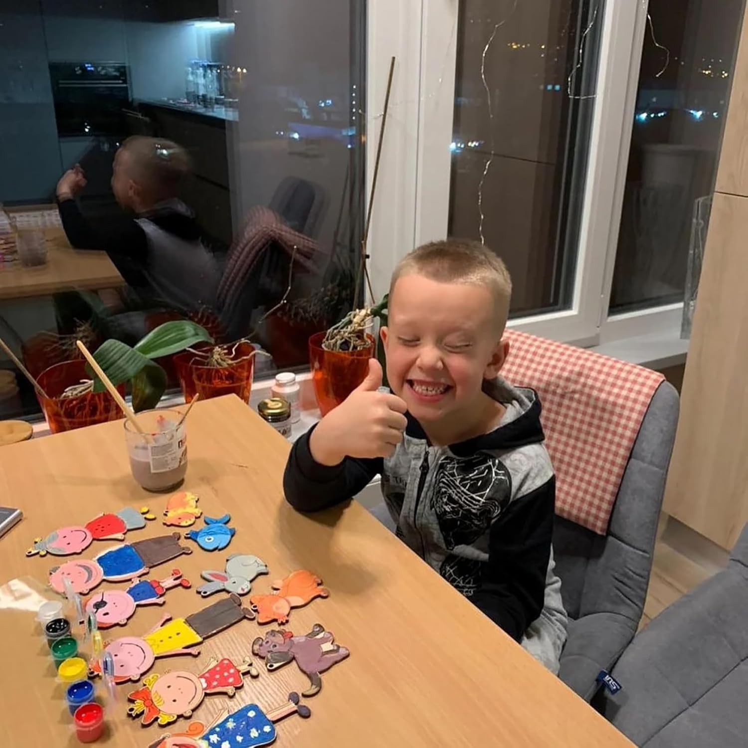 Child giving a thumbs-up at a table with craft materials