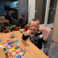 Child giving a thumbs-up at a table with craft materials