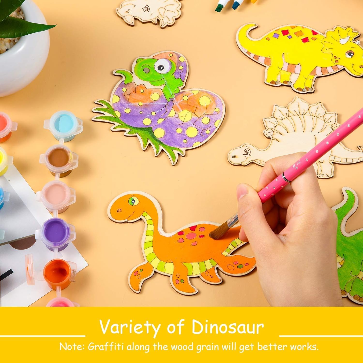 Colorful dinosaur-shaped wooden toys with a hand painting one of them on a yellow surface.