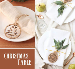 Decorative Christmas table setting with wooden ornament, white plates, and greenery.