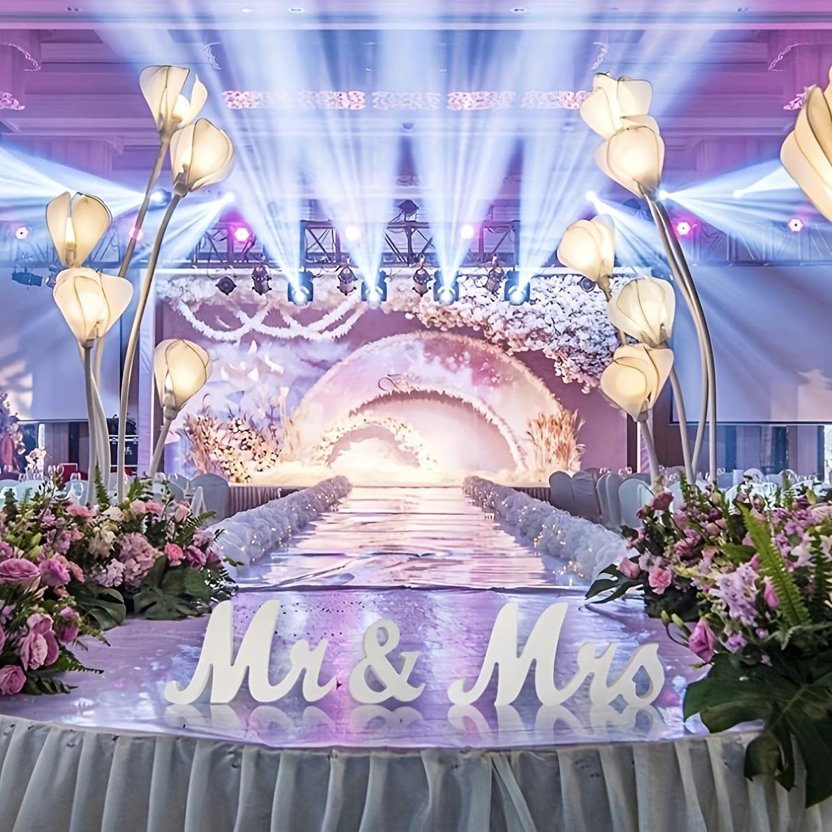 Decorated wedding stage with floral arrangements and 'Mr & Mrs' sign.