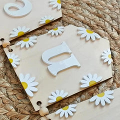 Wooden letters 'Q' and 'P' with daisy flower decorations on a woven mat.