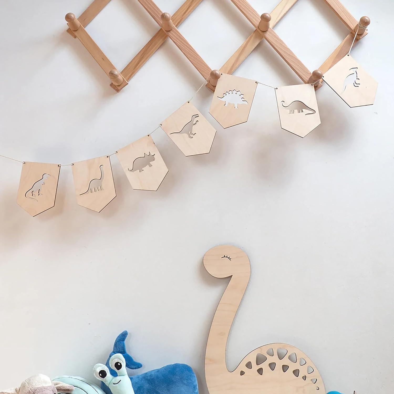 Wooden dinosaur banner with cut-out shapes on a white wall, accompanied by plush toys.