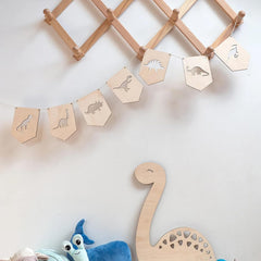 Wooden dinosaur banner with cut-out shapes on a white wall, accompanied by plush toys.