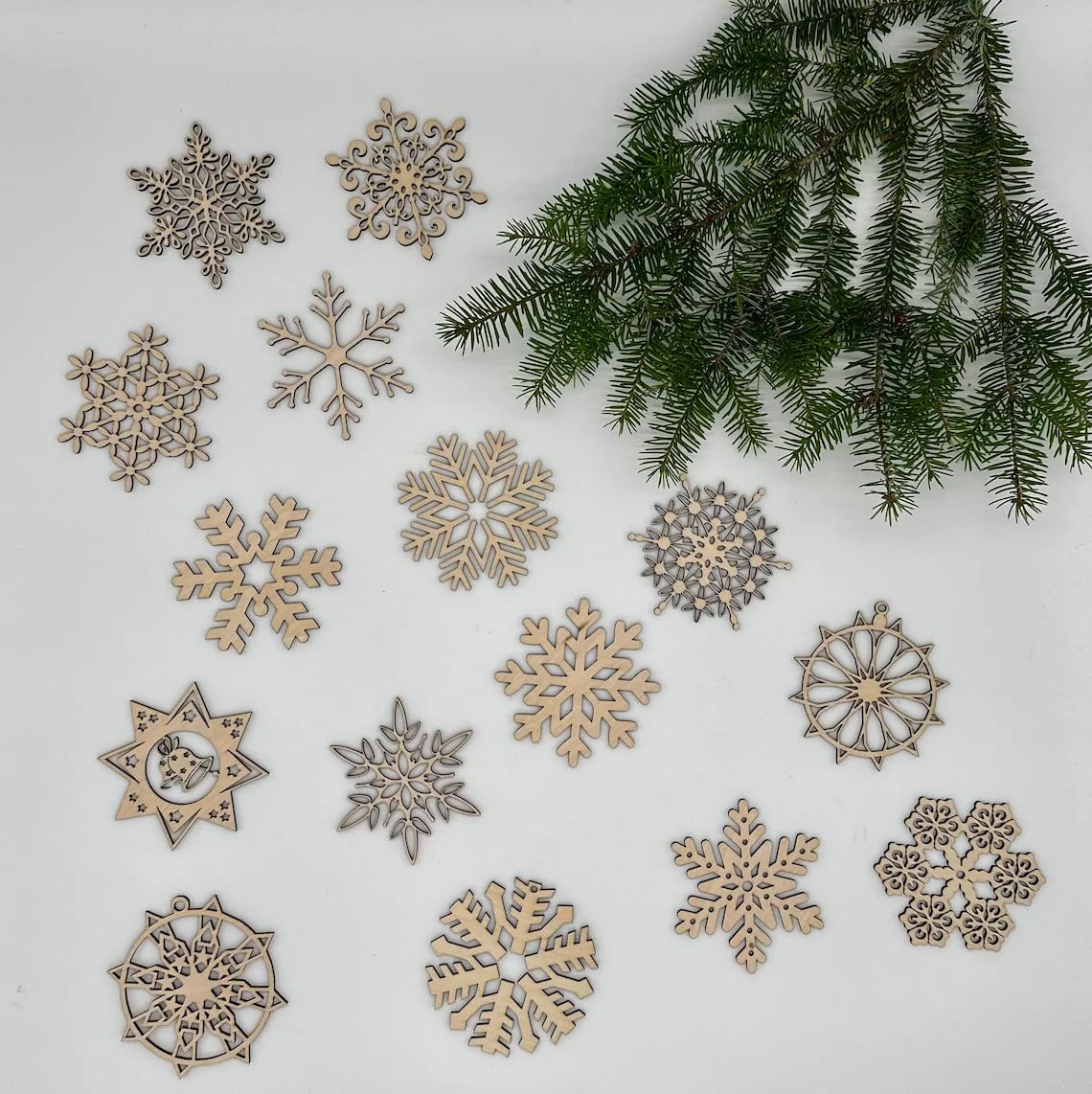 Decorative snowflake ornaments on a white surface with a branch of pine tree.