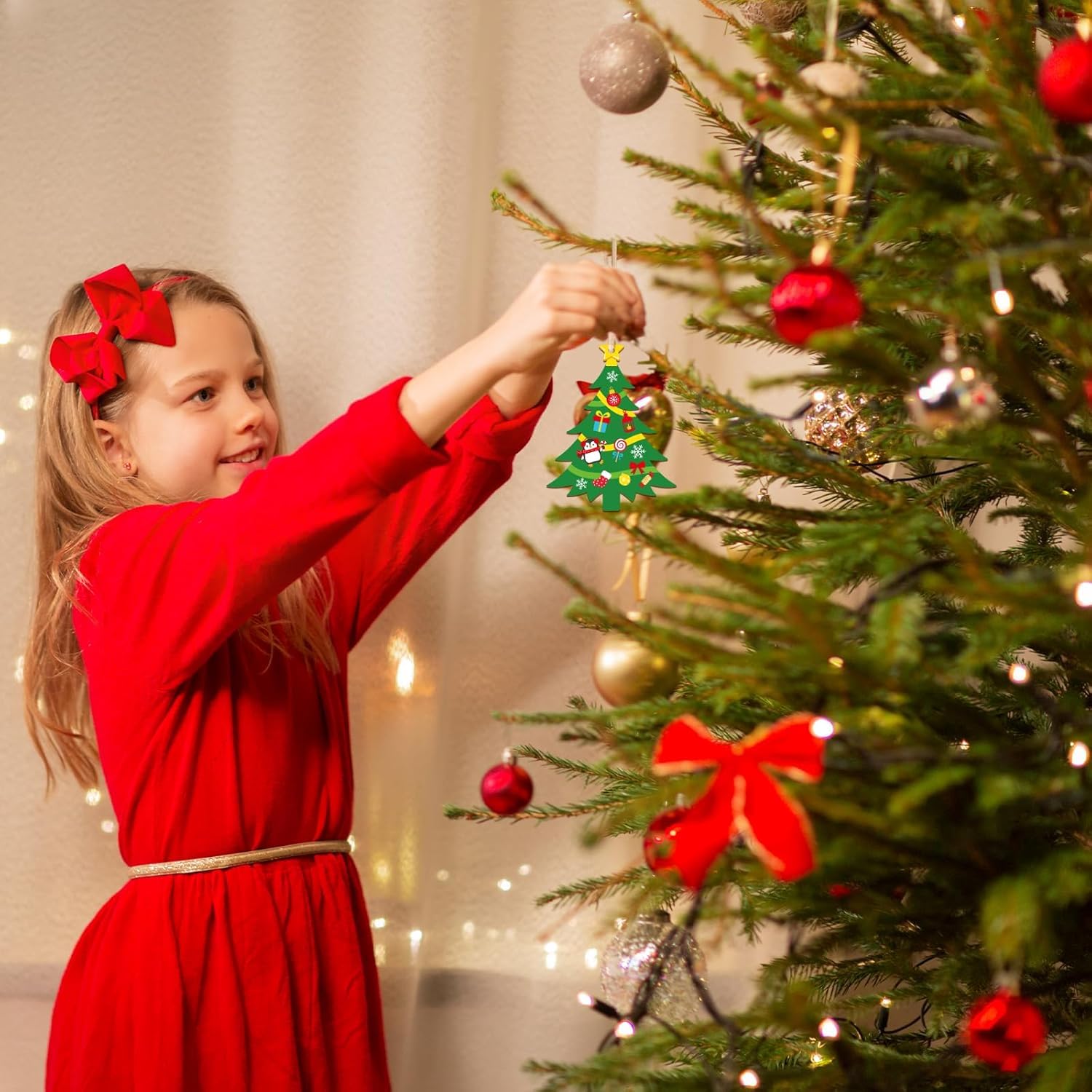 Child in a red dress decorating a Christmas tree with ornaments.