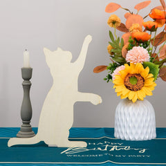 Cat-shaped decorative item, candle, and floral arrangement on a table with a 'Happy Birthday' mat.