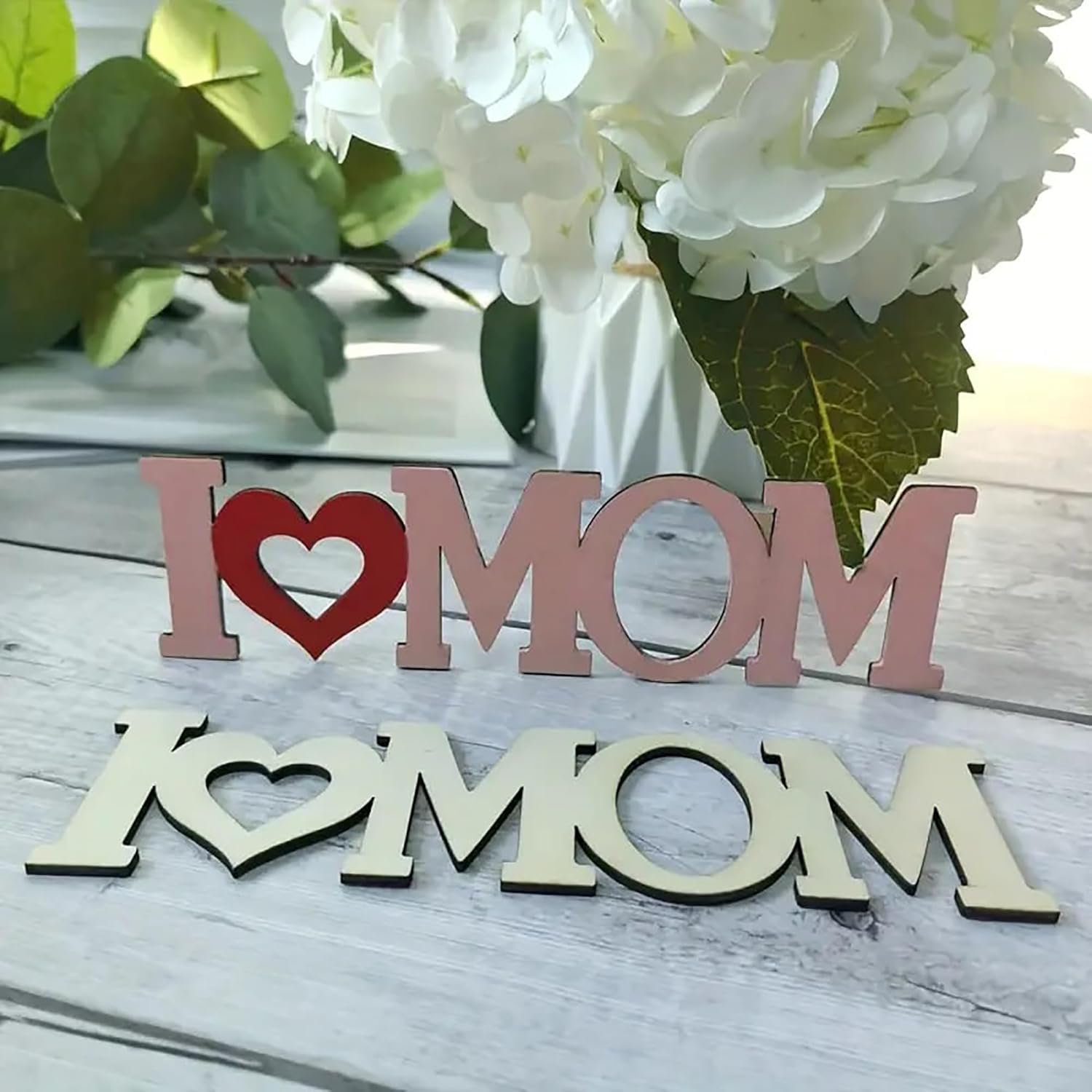 Wooden decorative sign with 'I ❤️ MOM' on a wooden surface with flowers in the background.