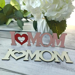 Wooden decorative sign with 'I ❤️ MOM' on a wooden surface with flowers in the background.