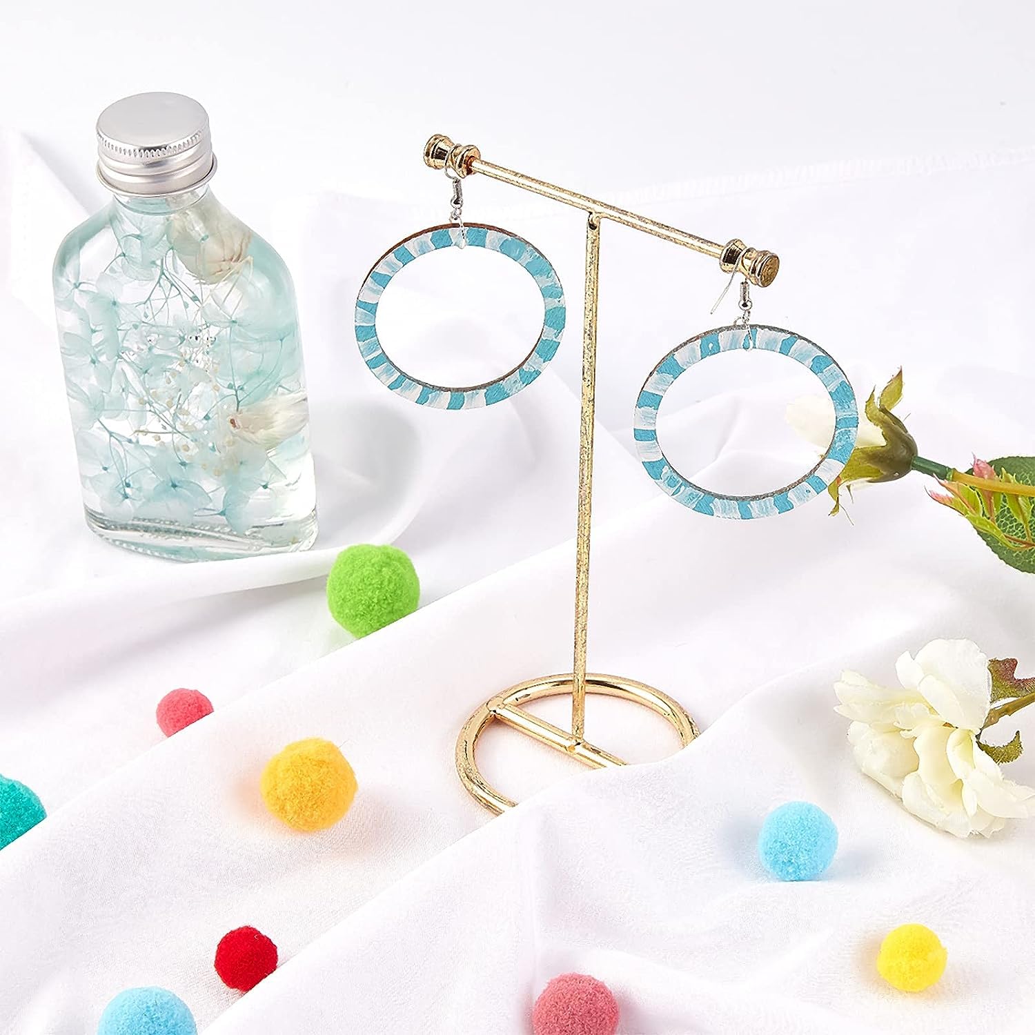 Earrings on a stand with a bottle of perfume and colorful pom-poms on a white background