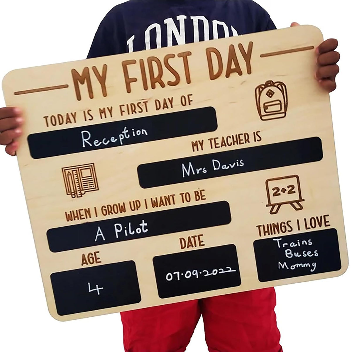 Wooden sign with engraved text for a child's first day of school, held by a person.