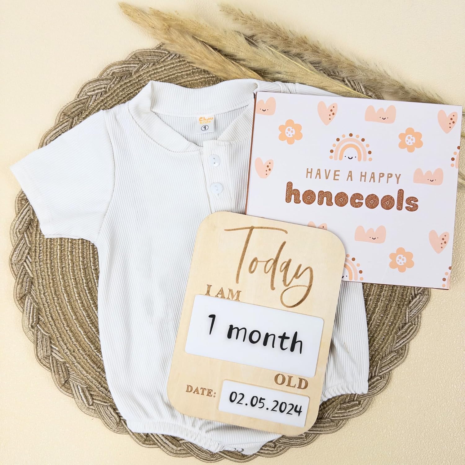 Baby onesie with milestone card and measuring stick on a woven mat