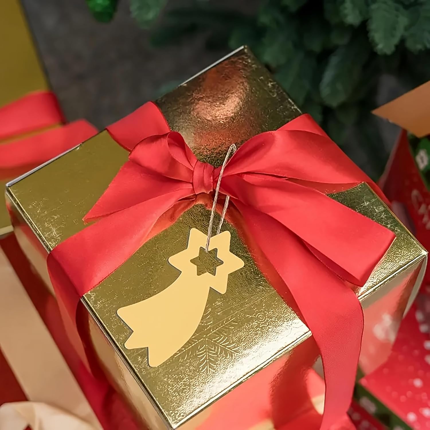 Gold gift box with a red ribbon and star-shaped tag, Christmas tree in the background