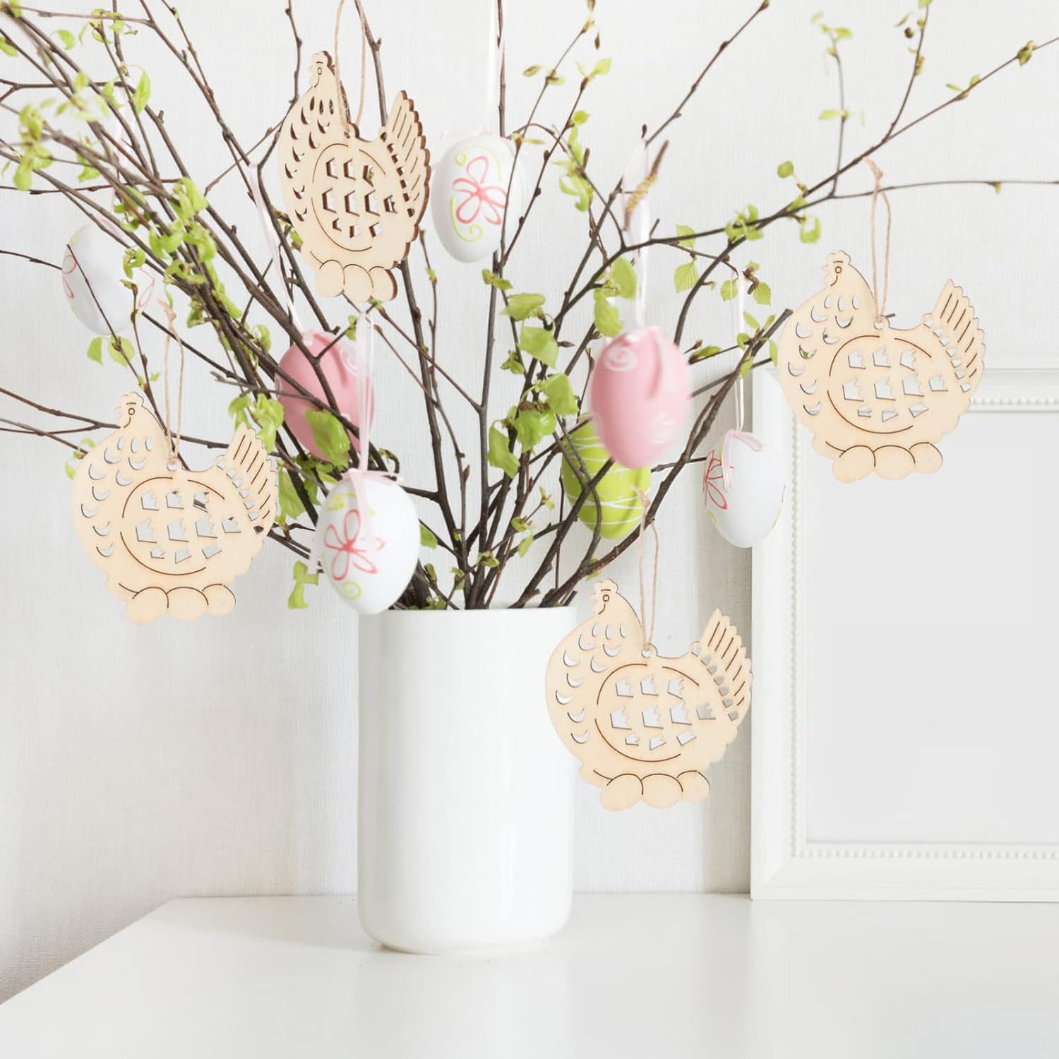 Decorative Easter arrangement with branches, eggs, and gold bird-shaped ornaments in a white vase.