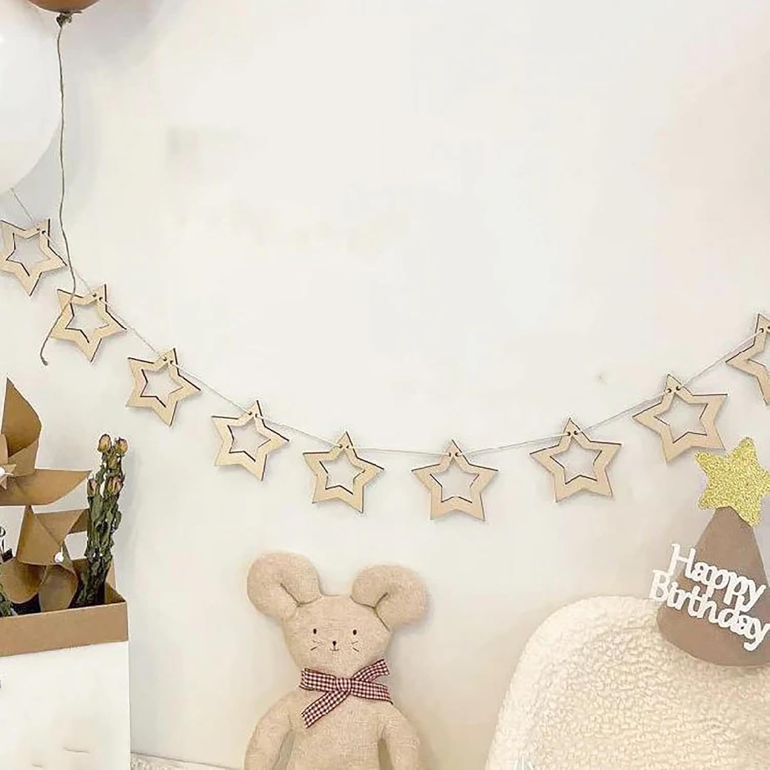 Decorative star garland with a teddy bear and 'Happy Birthday' sign on a white wall.