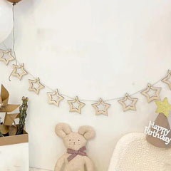 Decorative star garland with a teddy bear and 'Happy Birthday' sign on a white wall.