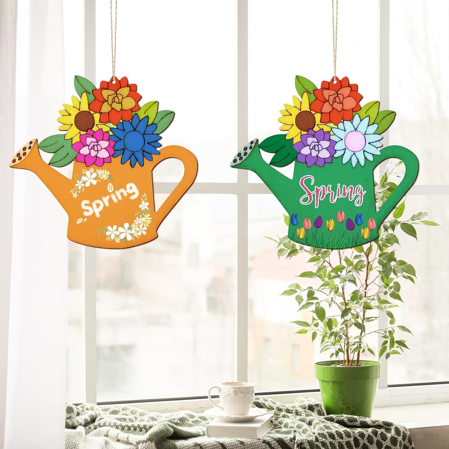 Two colorful watering can-shaped spring decorations with flowers on a windowsill.