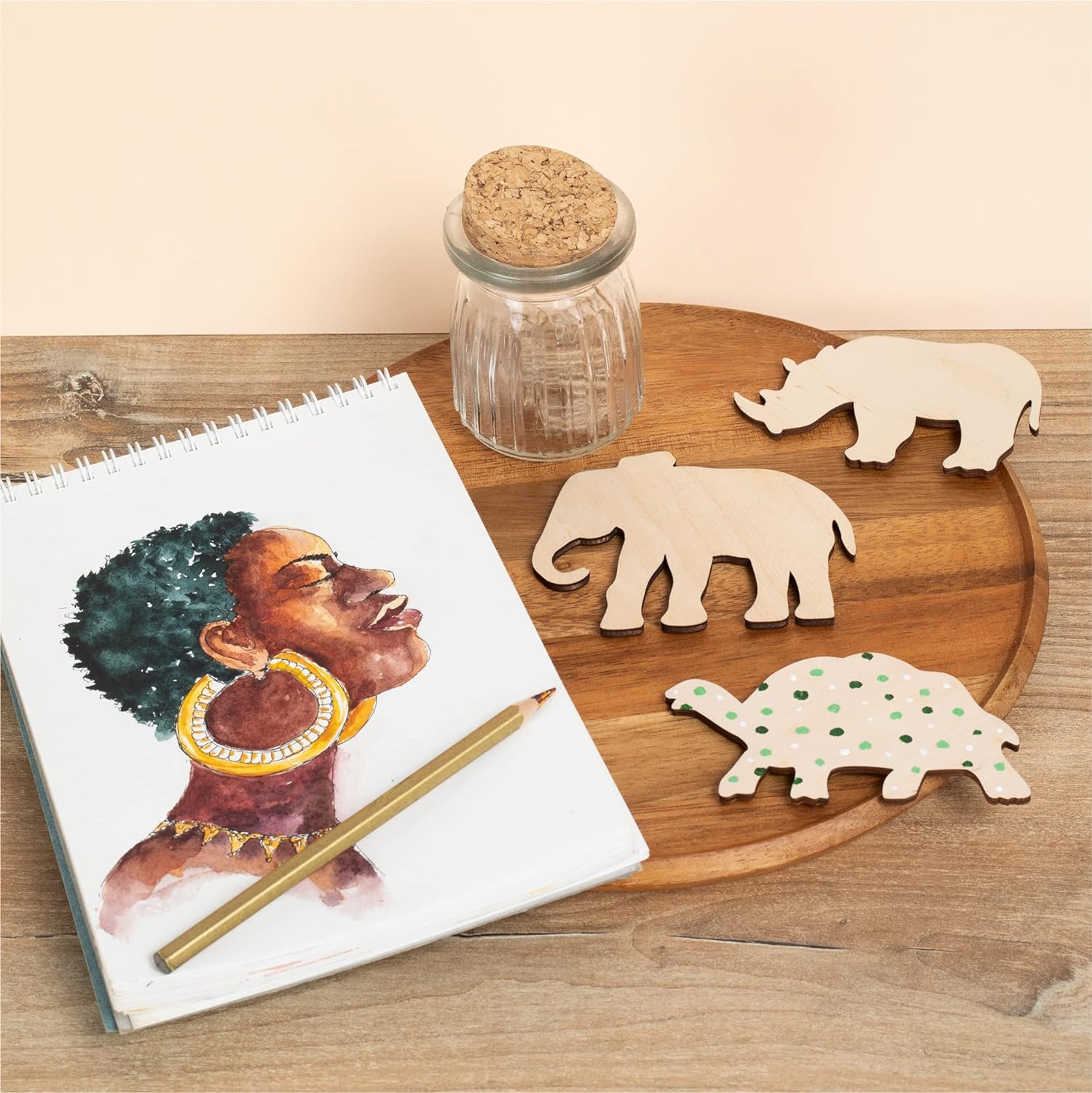 Wooden tray with animal cutouts, a notebook, and pencil on a wooden surface.
